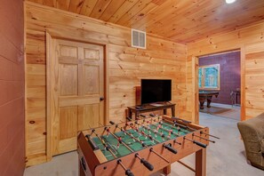 Una habitación con piso de madera, una mesa de fútbol de mesa, un televisor y una mesa de billar.