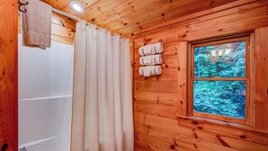 A wooden cabin bathroom with a bathtub, a shower curtain, and a window with a forest view. - Uncle Johns Cabin (Vilas)
