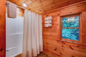 Baño de cabaña de madera con bañera, cortina de ducha y ventana con vista al bosque.