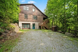 A two-story log cabin with a stone foundation, a gravel driveway, and a wooden deck. - Uncle Johns Cabin (Vilas)