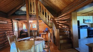 Interior de una cabaña de troncos con escalera, comedor, sala de estar y cocina.