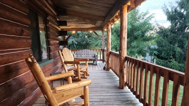 Una terraza de madera con mecedoras y un banco, rodeada por barandilla de madera.