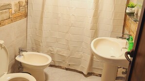 A bathroom with a toilet, bidet, and sink, tiled floor, and a shower curtain.