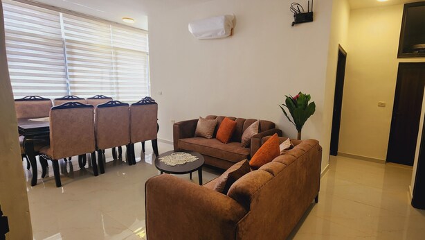 A living room with a brown sofa, a coffee table, and a dining area with chairs and a table.