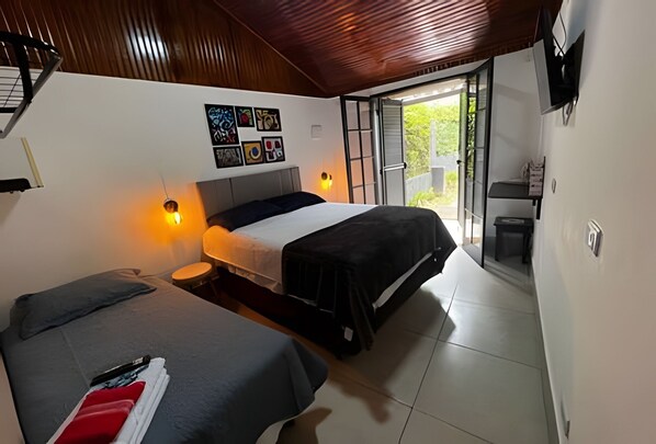 A bedroom with two beds, a wall-mounted TV, and a sliding door leading to a balcony.