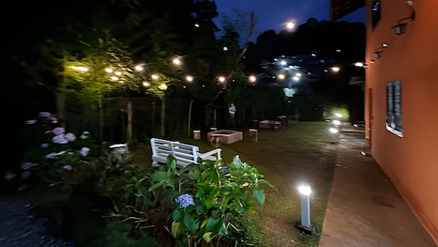 An outdoor garden area with string lights, a white bench, and a pathway leading to a building. - Fracalanza (Campos do Jordão)