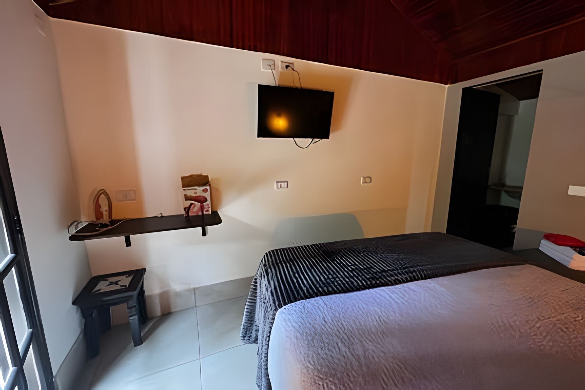 A bedroom with a bed, a TV mounted on the wall, a small table, and a chair.