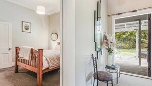 Ein Schlafzimmer mit einem hölzernen Bett, einem Sessel, einem Schreibtisch, einem großen Fenster und Blick ins Freie.