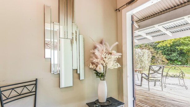 Ein Zimmer mit einem großen Spiegel, einer weißen Vase mit Blumen, einem Metallstuhl und einem kleinen Tisch mit einem dekorativen Gegenstand.