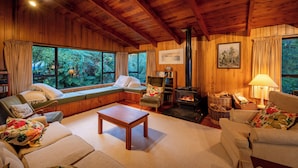 Een gezellig chaletinterieur met houten plafond, grote ramen, een open haard en comfortabele zitplaatsen.