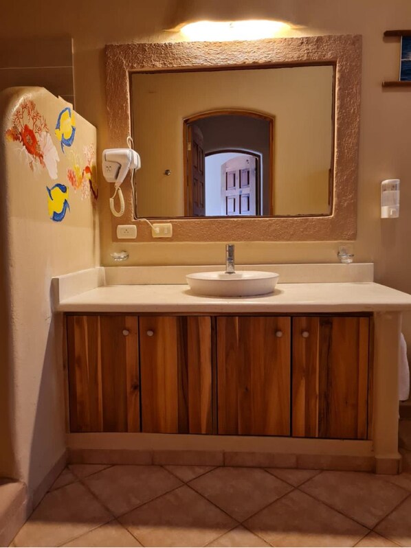 A bathroom with a wooden vanity, a white sink, a hairdryer, and a mirror with a textured frame. - Beautiful 1BR in front of the beach with pool spa restaurant (Las Terrenas)