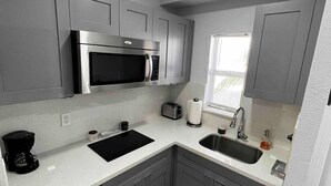 Eine moderne Küche mit grauen Schränken, einer Edelstahl-Mikrowelle, einem Toaster, einer Kaffeemaschine und einem Fenster, das für natürliches Licht sorgt.