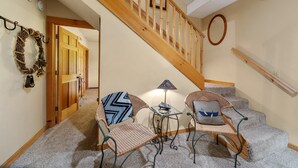 A staircase with wooden railings, a small table with a lamp, two wicker chairs with cushions, and a wall-mounted mirror. - Appalachian Satisfaction (Banner Elk)