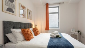 Ein ordentlich bezogenes Bett mit weißen und orangefarbenen Kissen, einer blauen Decke und einem weißen Kopfteil.