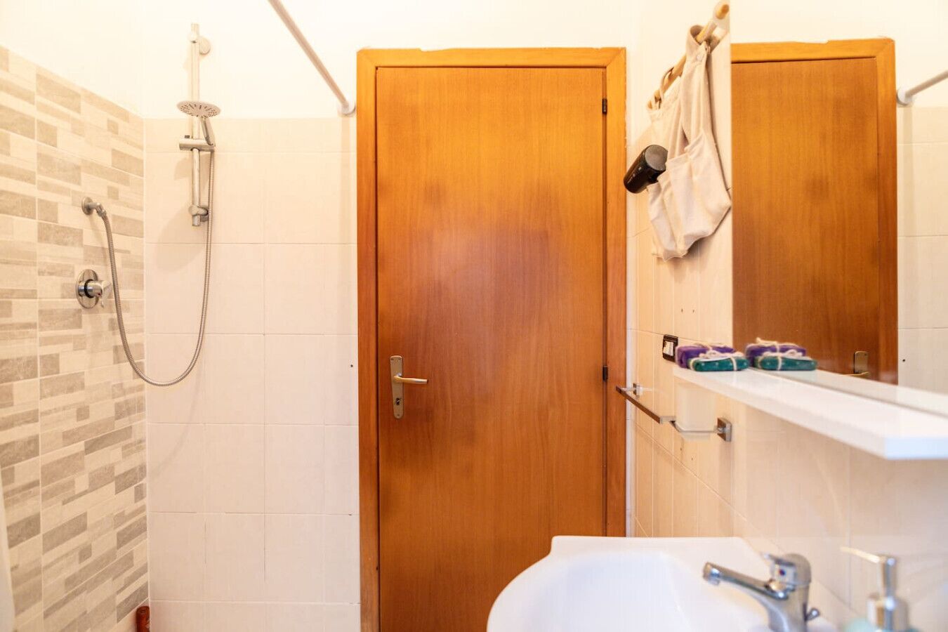 A bathroom with a shower, wooden doors, a sink, and a towel rack with towels.