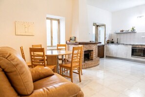 A modern living room with a leather sofa, wooden dining table, and chairs, a fireplace, and a kitchen with white cabinets and appliances. - Casa Frida - Roccagloriosa (Roccagloriosa)