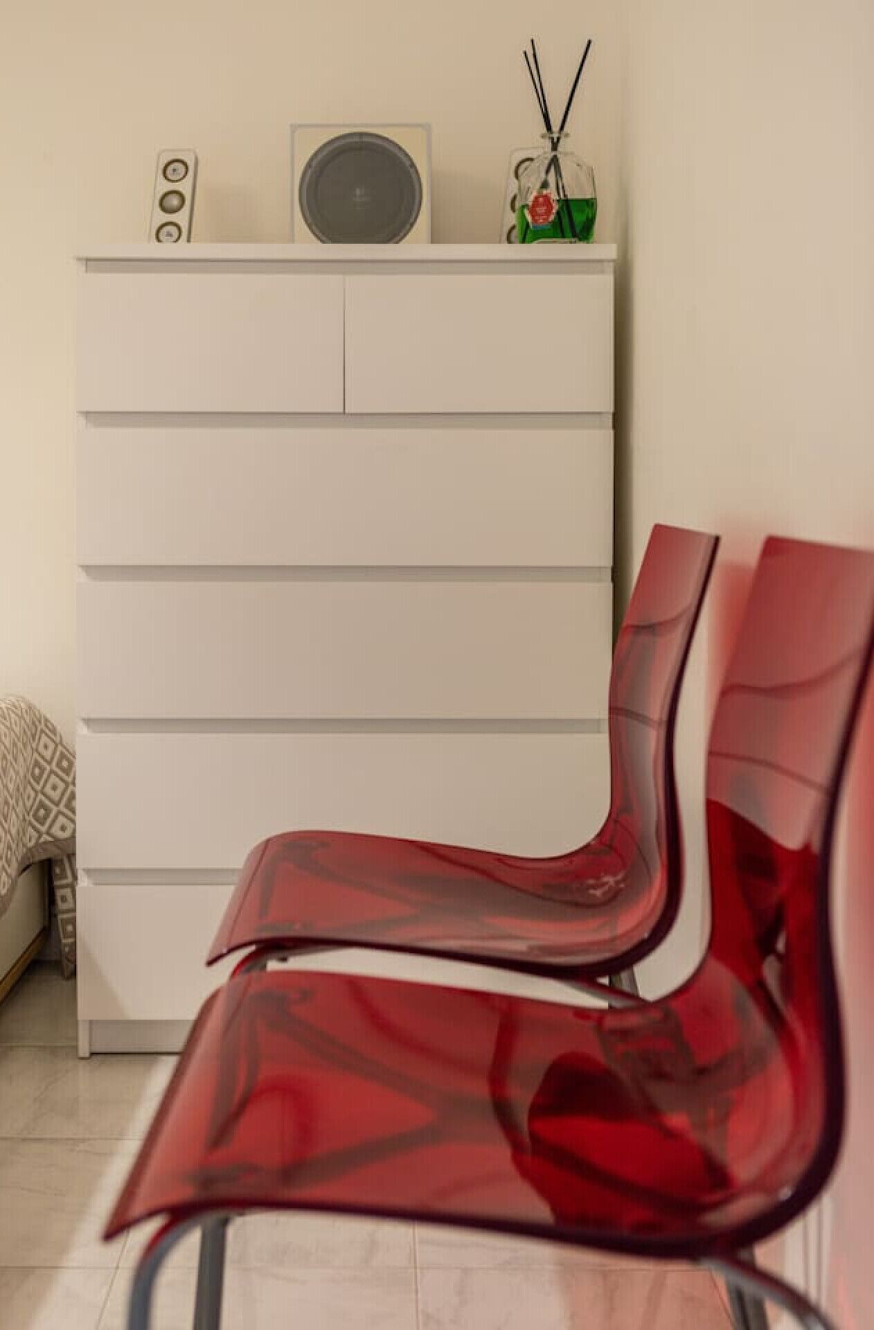 Een kamer met een witte dressoir, een rode stoel en een kleine tafel met een radio en een decoratief object.