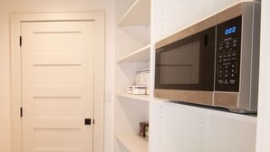 A kitchen with white shelving, a microwave, and a white door.