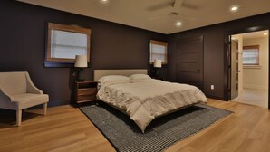 A modern bedroom with a large bed, a chair, two bedside lamps, and a ceiling fan.
