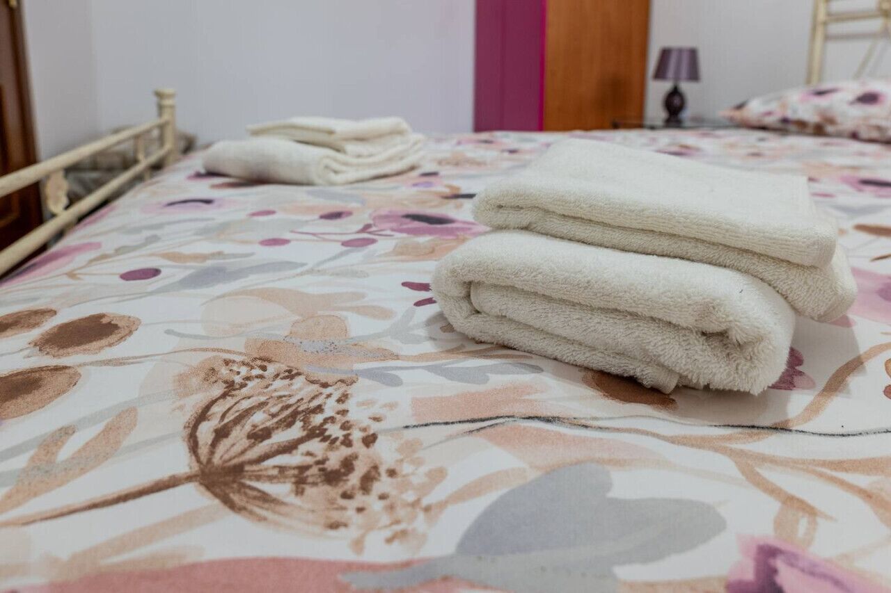 Een bed met een bloemenprintdeken en een stap witte handdoeken erop.