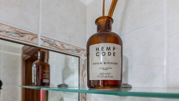 A bottle of 'HEMP CODE' room diffuser on a glass shelf in a bathroom with tiled walls.