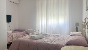 Un dormitorio con cama, dos mesitas de noche, una lámpara y una ventana con cortinas.