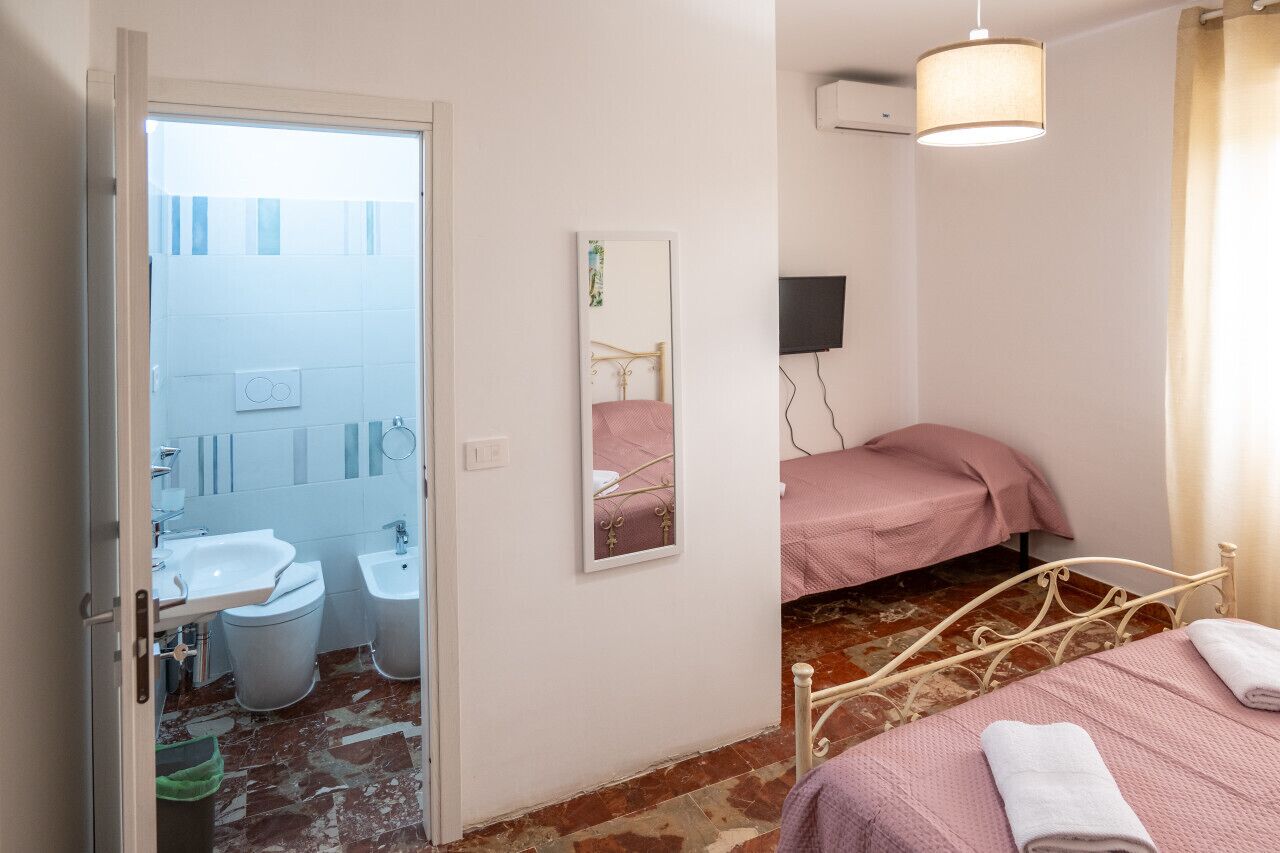 Un dormitorio con cama, mesita de noche, espejo y ventana.
