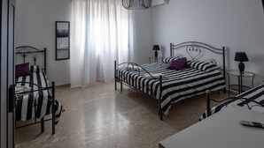 A bedroom with two beds, a bedside table with a lamp, a chair, a window with curtains, and a ceiling light fixture. - Villa D`Angelo - Quadrupla (Miracoli)