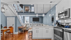 Una cocina moderna con una isla central, electrodomésticos de acero inoxidable y una escalera que sube a un nivel superior.