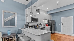 Una cocina moderna con una isla central, electrodomésticos de acero inoxidable y una escalera al fondo.
