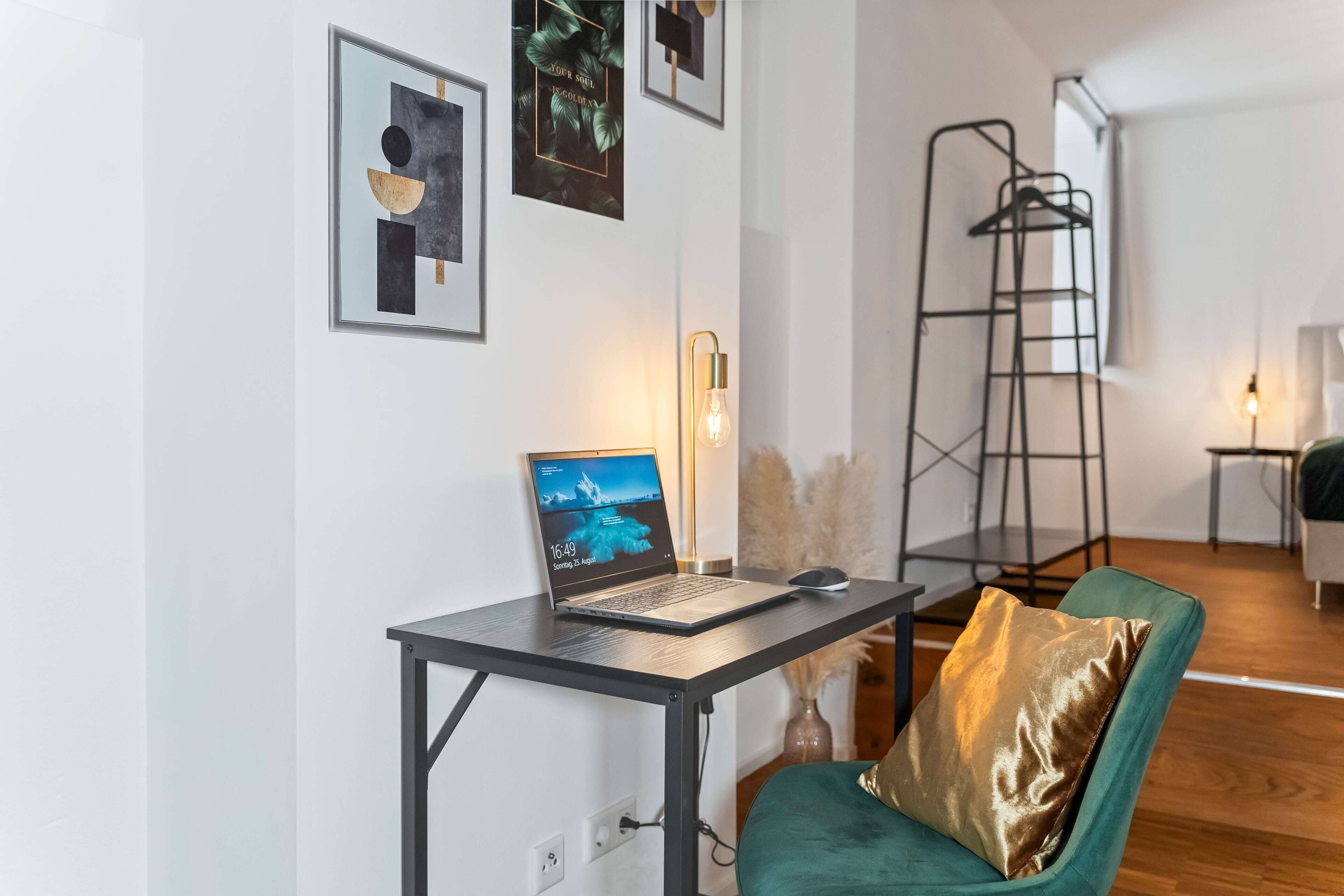 Een moderne kamer met een bureau, een laptop en een groene stoel met een gouden kussen.