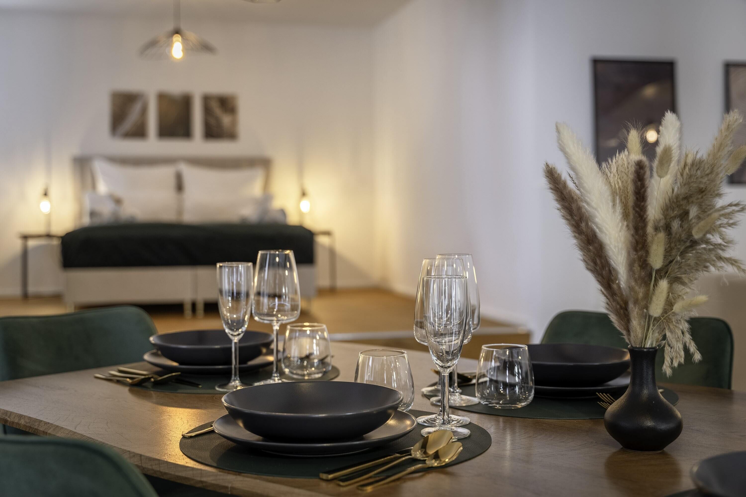 Een eettafel gedekt met zwarte borden, heldere glazen en bestek, met pampa'sgras in een vaas.