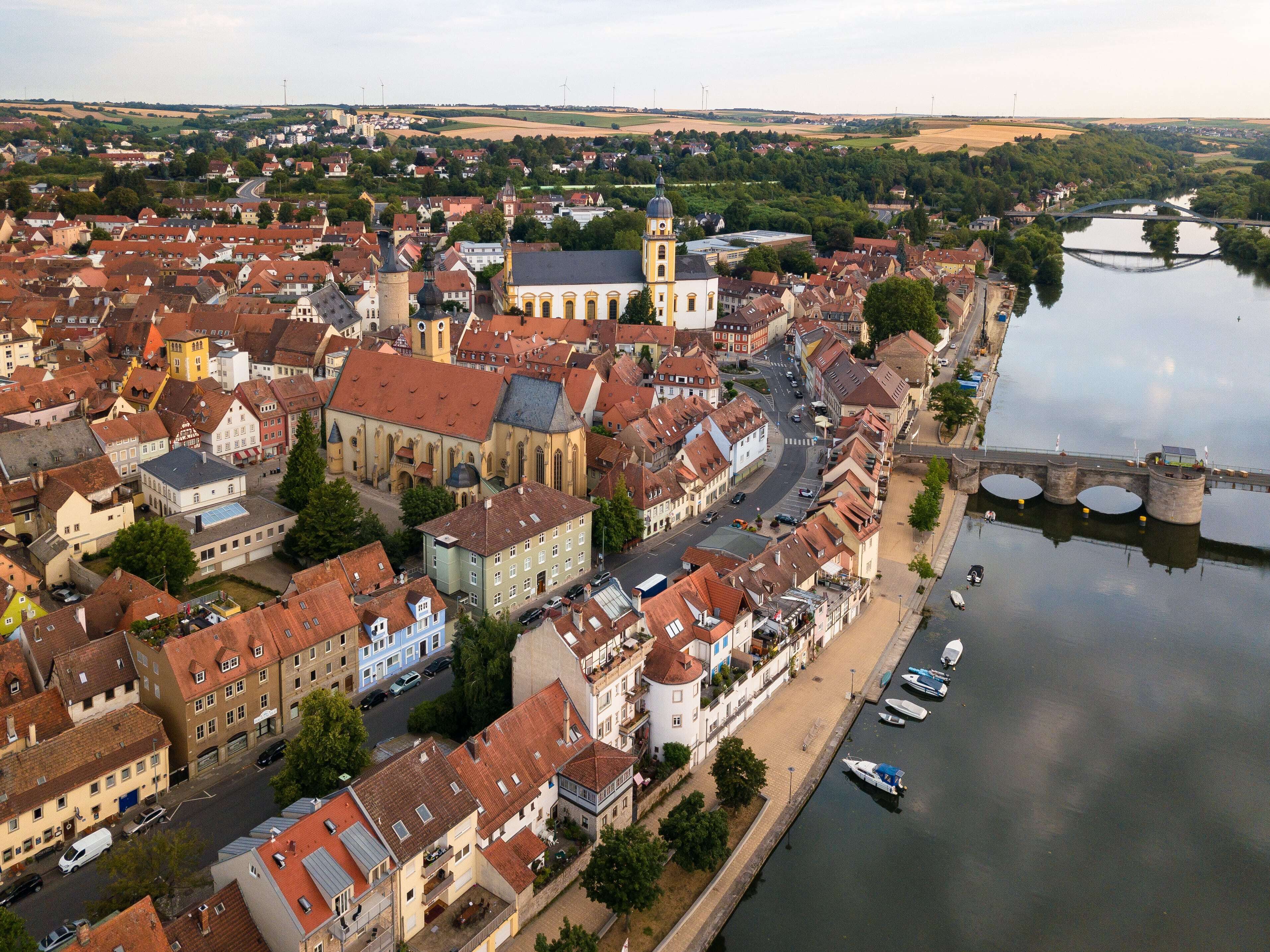 A riverside town with historic buildings, a prominent church, and a bridge over the river.