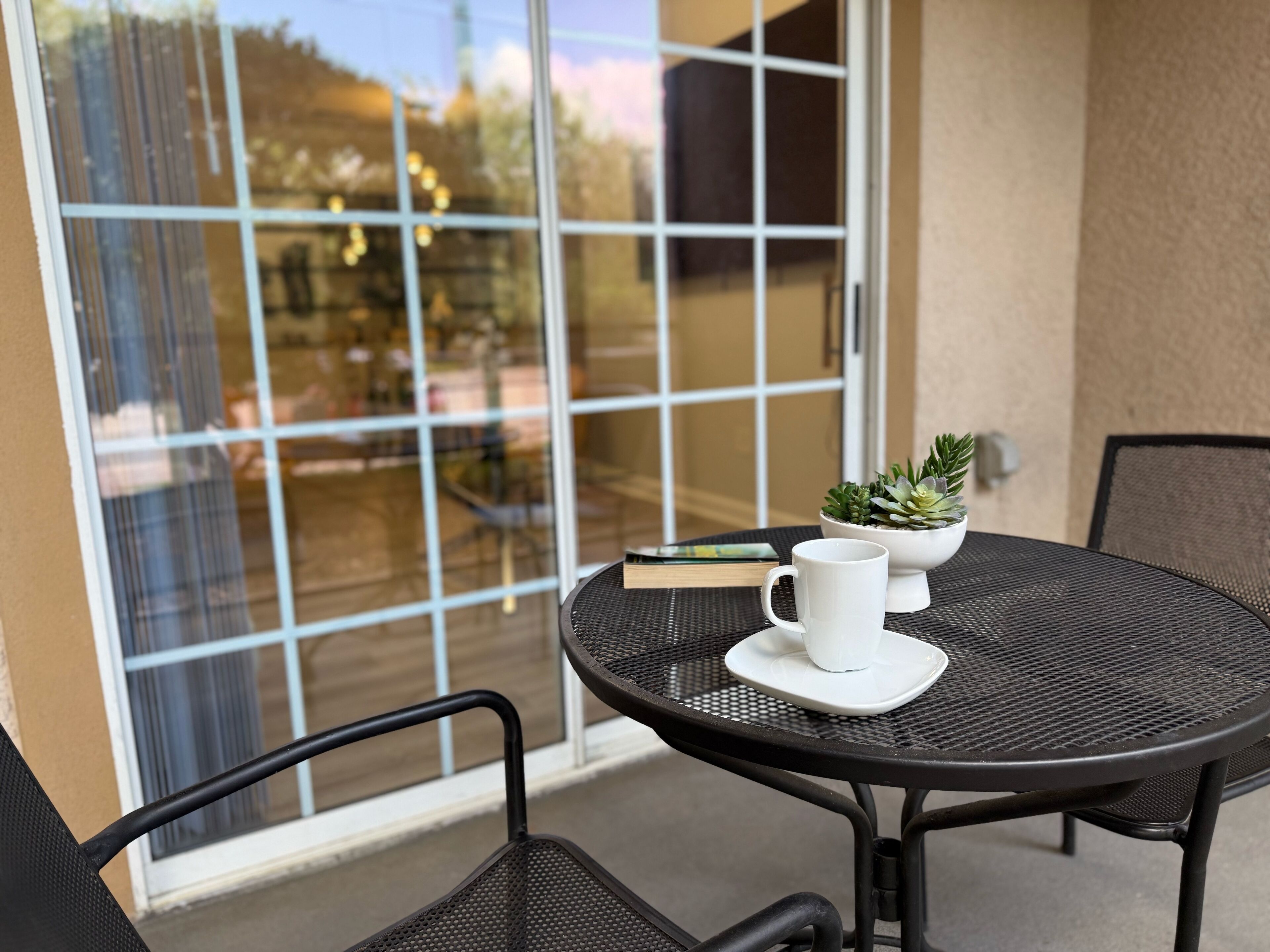 Une table ronde d’extérieur, sur laquelle sont posés un mug blanc et une petite plante en pot, entourée de chaises noires.