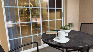 Une table ronde d’extérieur, sur laquelle sont posés un mug blanc et une petite plante en pot, entourée de chaises noires.