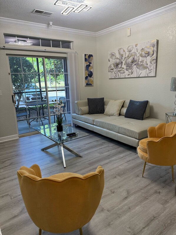 Relax in this stylish living room with a sofa, armchairs, and a coffee table, offering a view of the outdoors through a sliding glass door.