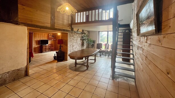 A spacious room with a wooden floor, a dining table, and a staircase leading to an upper level. - Aux Songes D'élise, Une, Maison Familiale au Coeur du Plateau des Mille Étangs (Belmont)