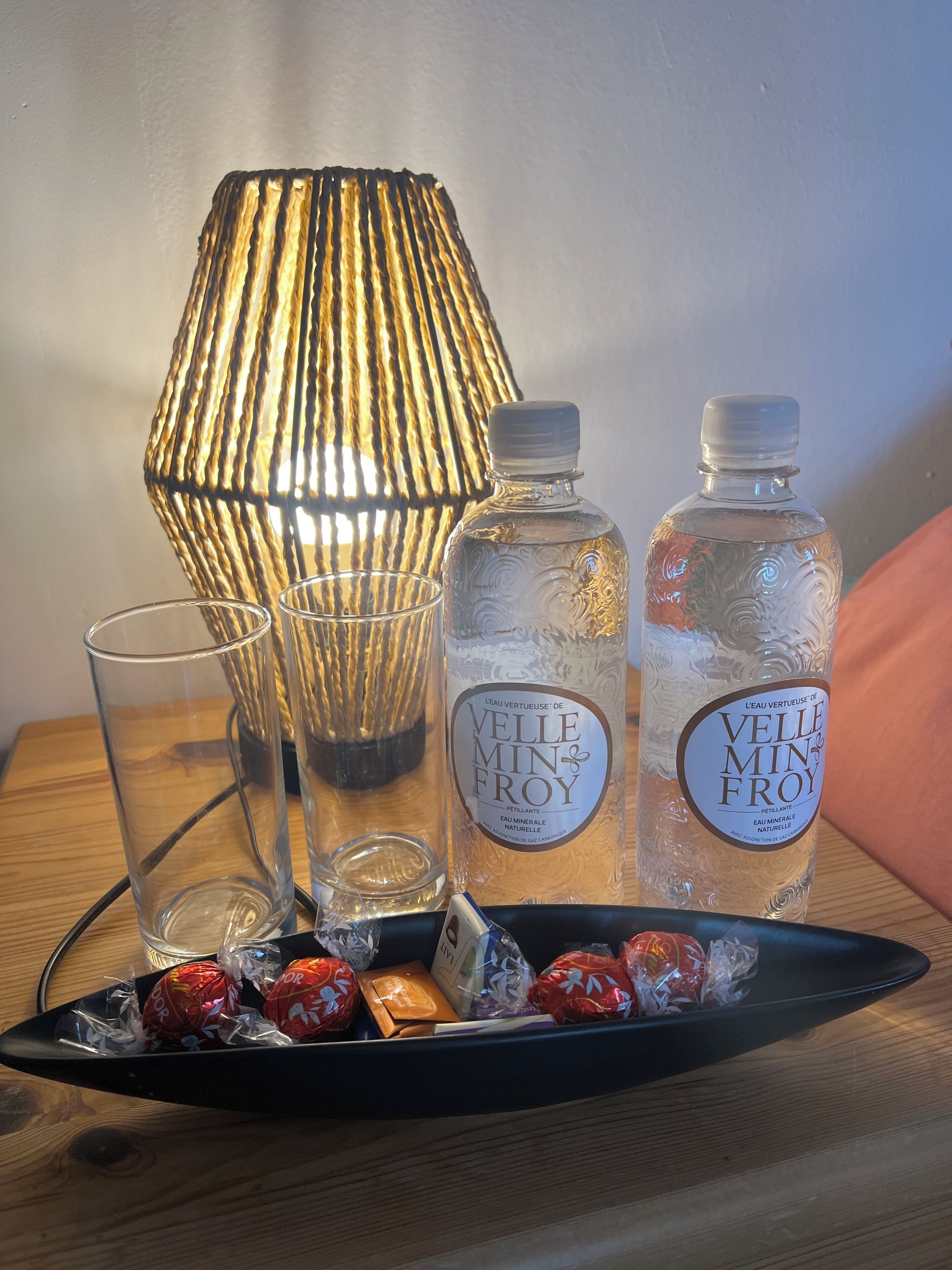Ein Tisch mit zwei Wasserflaschen, einem Glas und einer Platte mit verpackten Pralinen.