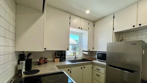 Una cocina moderna con armarios blancos, un refrigerador de acero inoxidable, un microondas, una estufa y una ventana que proporciona luz natural.