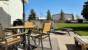 Un patio exterior con una mesa, sillas, una parrilla y un gran paraguas.