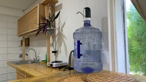 A kitchen with a large water dispenser, a stove, and a window with a view of greenery. - Casa Samay Cozumel (Cozumel)