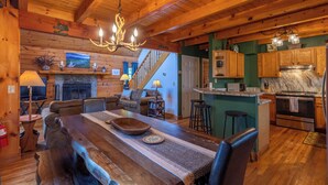 L’intérieur d’un chalet rustique comprend une table à manger en bois, une cheminée, un coin cuisine et un escalier menant à un autre niveau.