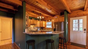 Une cuisine avec des poutres en bois, un grand îlot central avec des tabourets et un réfrigérateur.