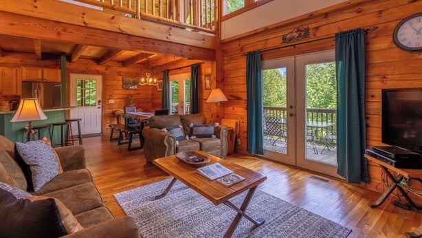 Un vaste salon au décor intérieur en bois, un coin repas et un balcon offrant une vue sur l’extérieur.