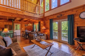 A spacious living room with a wooden interior, a dining area, and a balcony with a view of the outdoors. - Hillside Heaven (Boone)