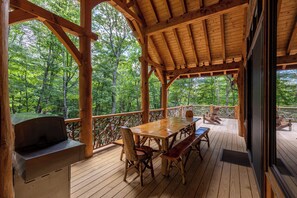 Une terrasse en bois, agrémentée d’une table et de chaises, entourée d’une rambarde et offrant une vue sur une zone boisée.