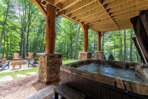 Un bain à remous sous une pergola en bois, entouré de piliers en pierre, avec des chaises et un banc en pierre à proximité.