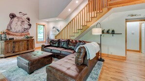 A spacious living room with a large sectional sofa, a wooden staircase, and a bear mural on the wall. - Paws A While (Blowing Rock)