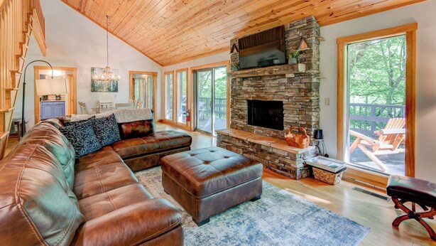 A cozy living room with a stone fireplace, leather sofa, and large windows. - Paws A While (Blowing Rock)
