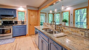 A modern kitchen with granite countertops, stainless steel appliances, and large windows offering a view of the outdoors. - Paws A While (Blowing Rock)